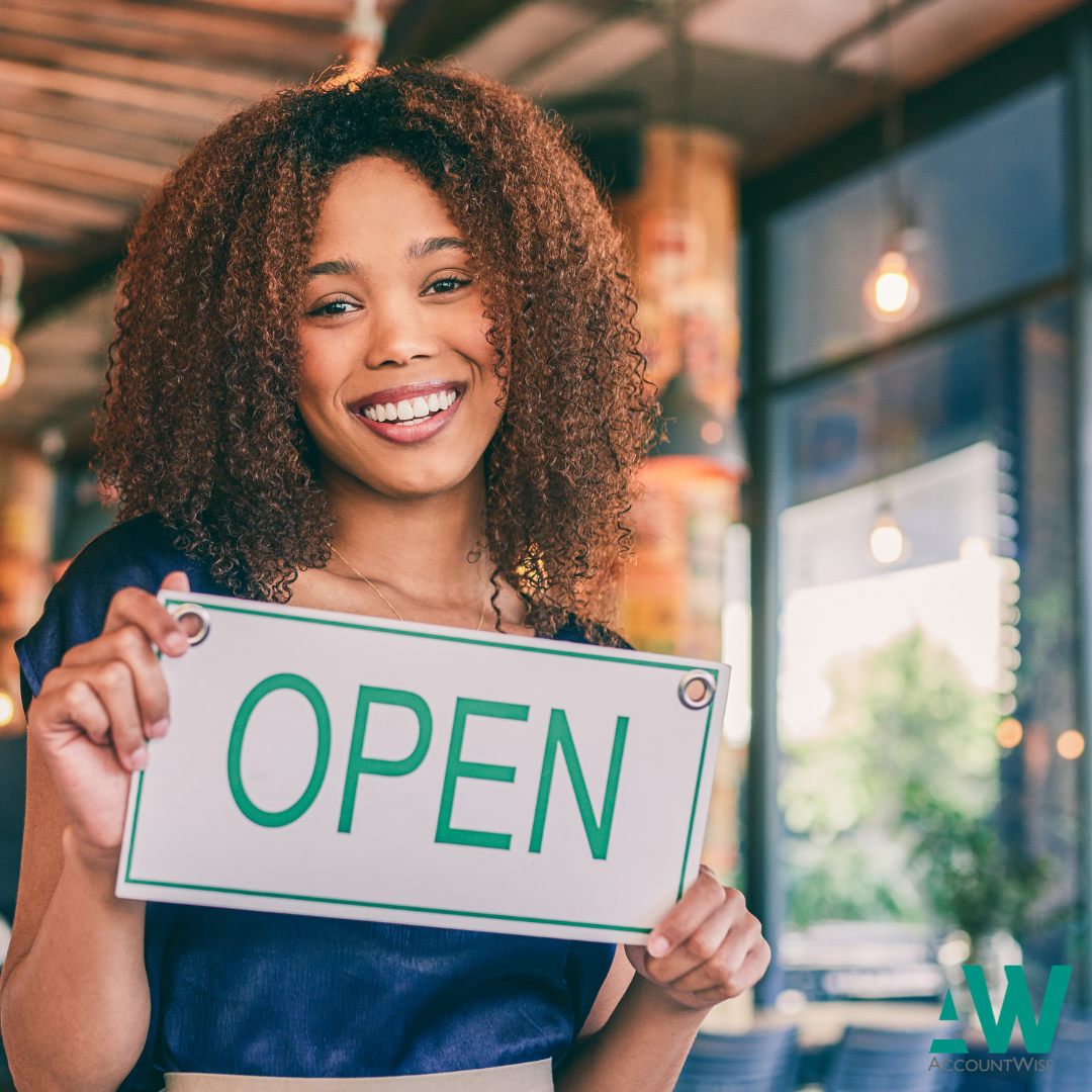 A lady who has just started a business as a sole trader holding a sign saying 'open'